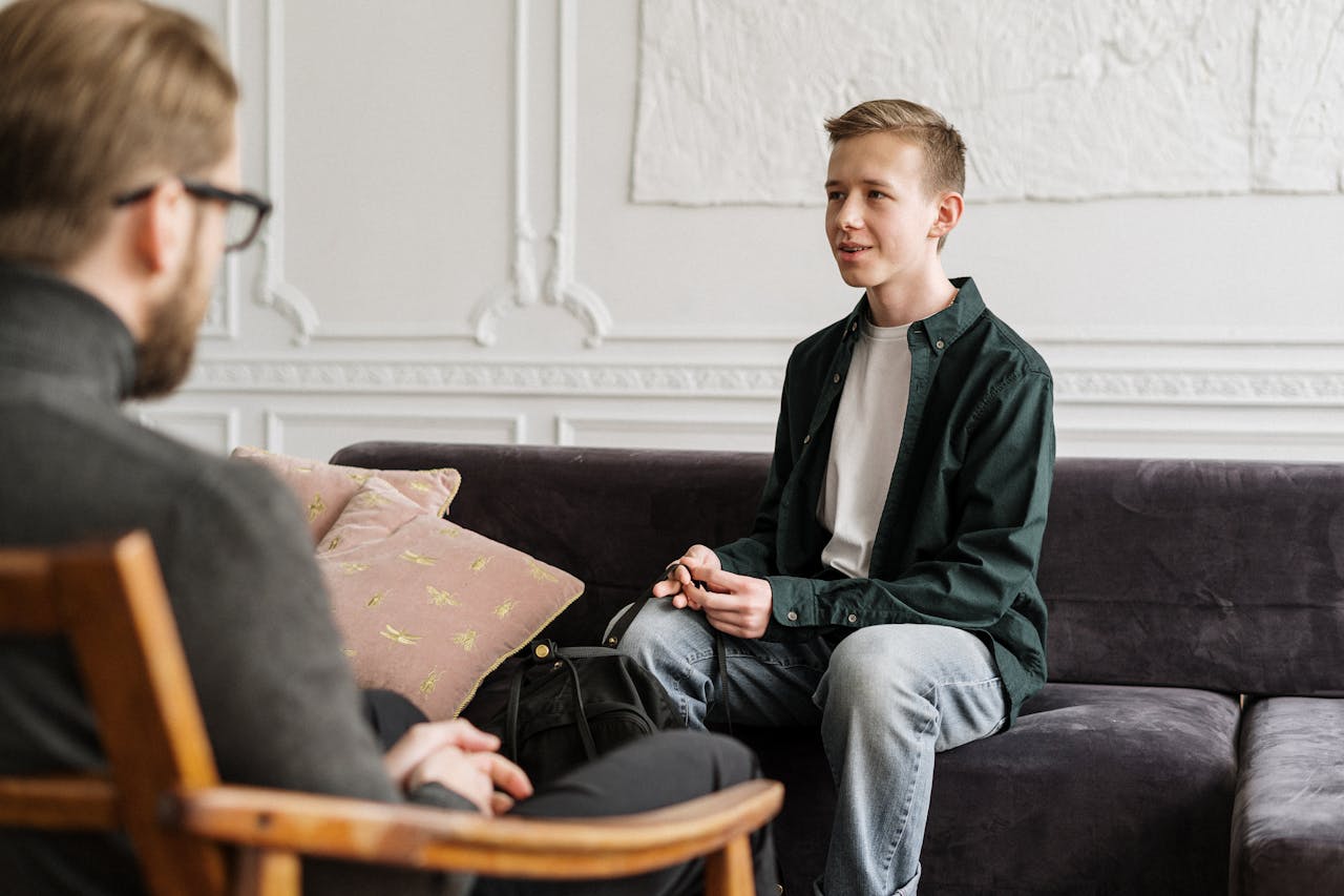 A teenage boy in a counseling session discussing with a therapist in an office setting.